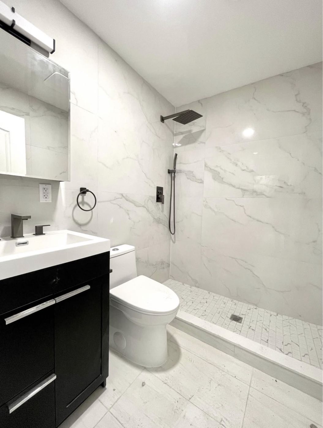 Private master bathroom with floor-to-ceiling marble tile, rain shower, and matte black fixtures